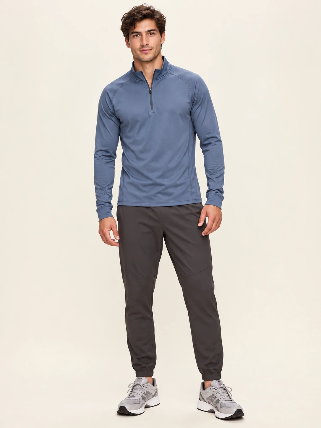 Male model wearing a blue quarter-zip long sleeve performance top with dark jogger pants for men’s custom gymwear