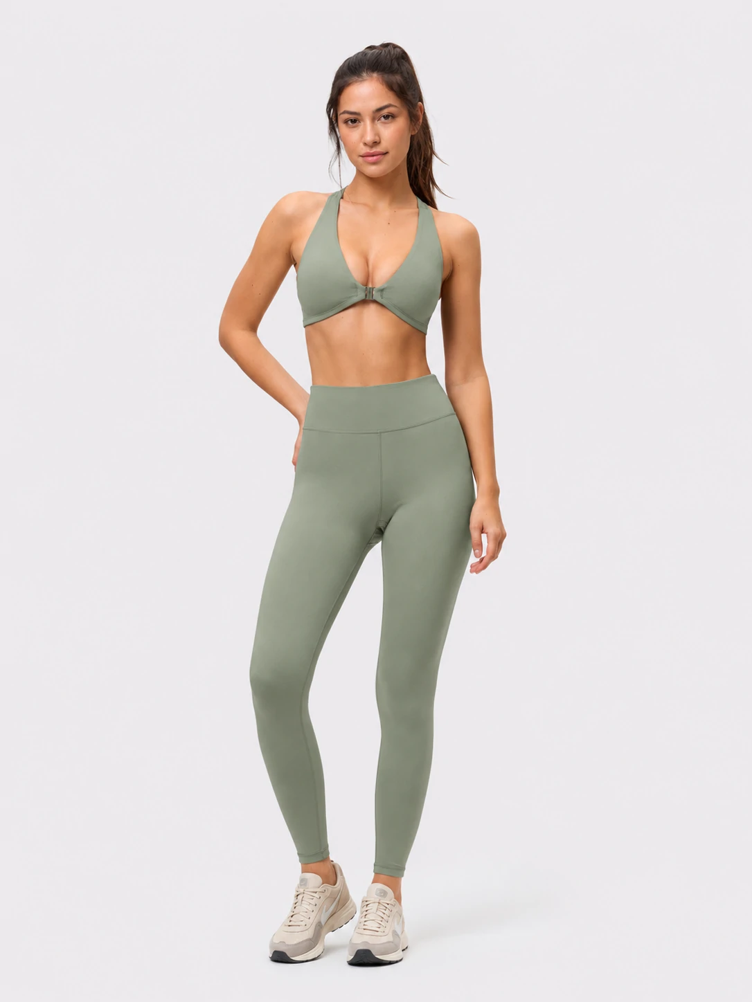 Female fitness model wearing a sage green sports bra and high-waisted leggings for custom women’s activewear
