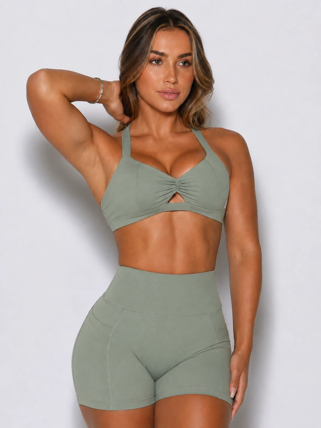 Female fitness model wearing a custom sage green sports bra and high-waisted gym shorts activewear set
