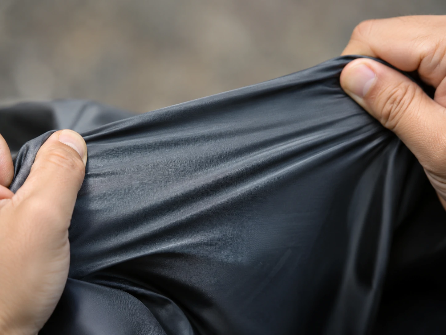 Hands stretching black performance fabric to demonstrate elasticity, flexibility and durability for custom activewear production