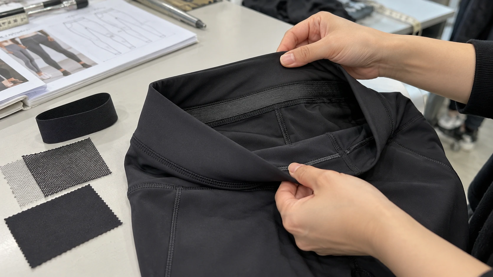 Close-up quality inspection of black activewear leggings waistband, elastic construction and seam finishing during product development